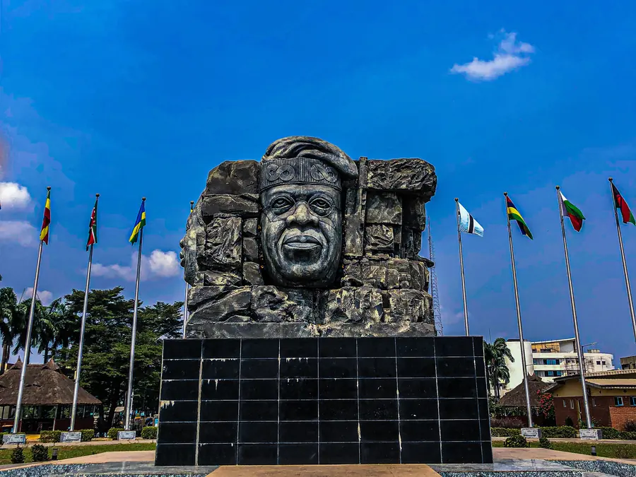 A sculpted stone monument ringed by flags at Johnson Jakande Tinubu Park